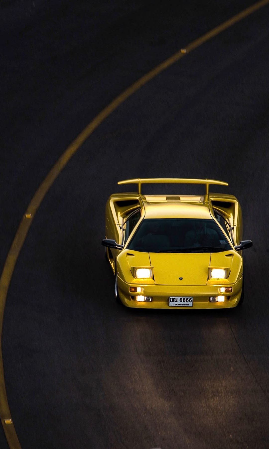 Yellow Lamborghini Diablo on a dark road, headlights on, seen from above
