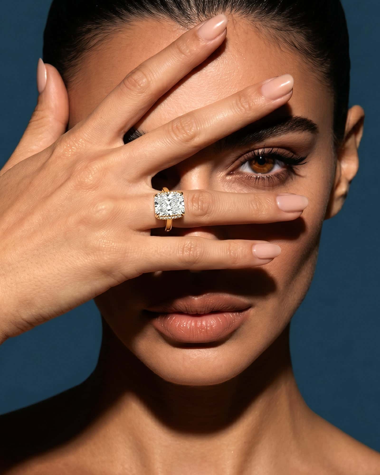 Doenara: a diamond ring on a hand held across a face, deep blue backdrop