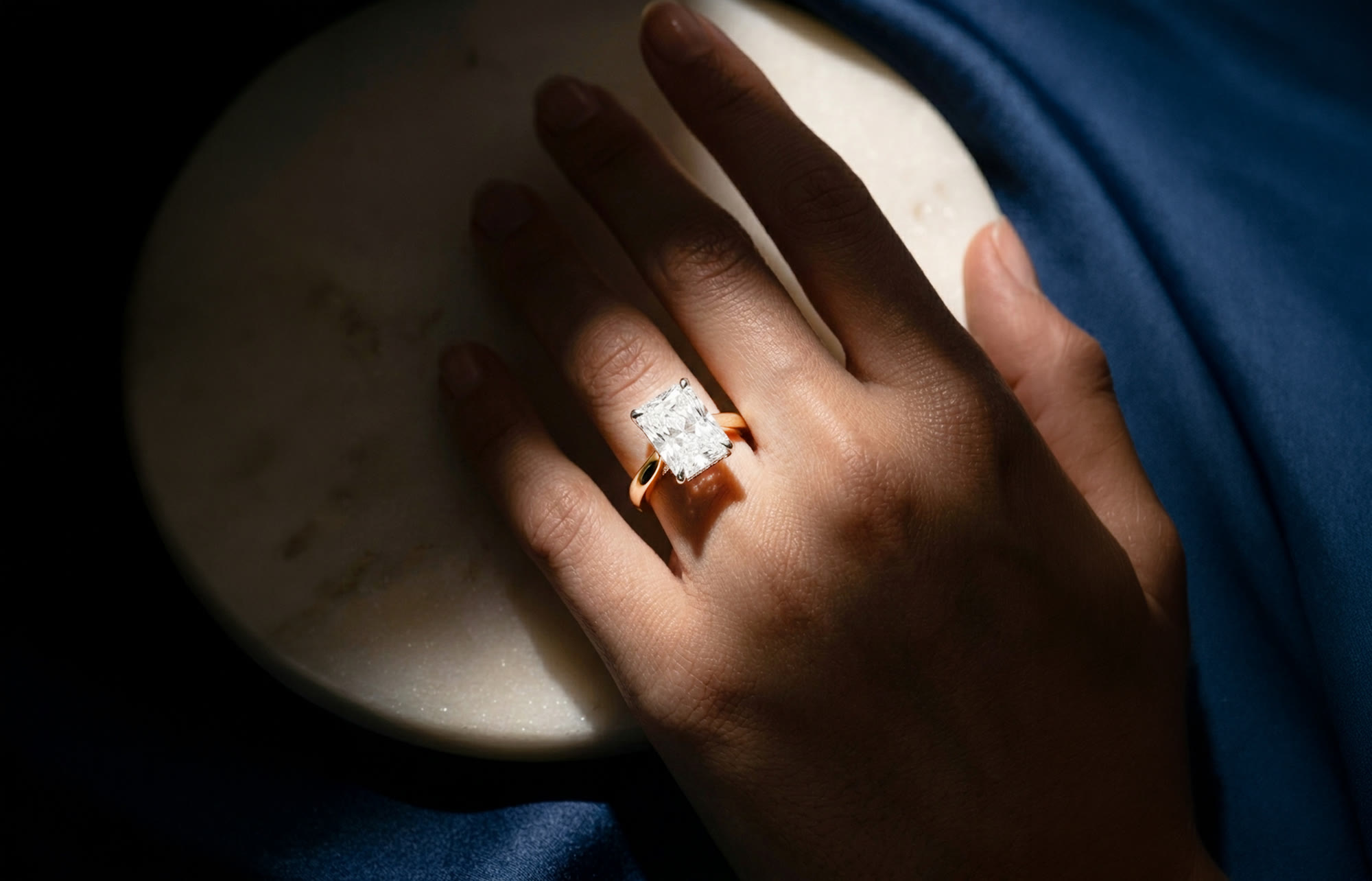 Doenara: a diamond ring on a hand resting on marble and blue cloth